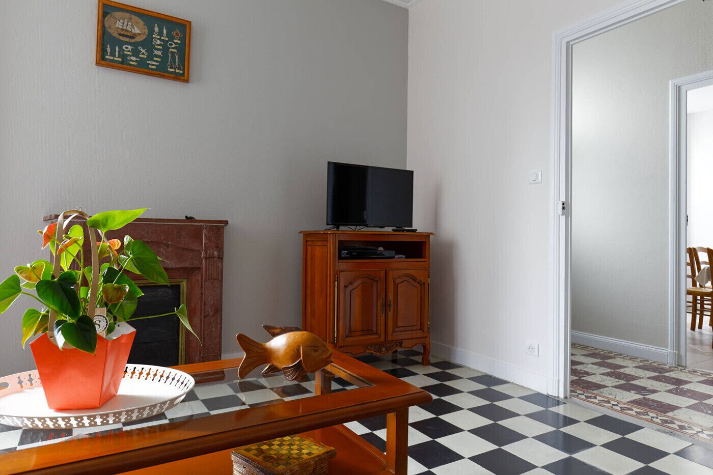 Ein Wohnzimmer mit Schachbrettboden, einem Holzschrank mit Fernseher, einem Kamin und einer Pflanze auf einem Tisch.