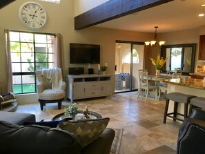 A spacious living room with a large clock, a television, and a dining area with a kitchen visible through an archway. - Beautiful courtyard villa at the Pointe Resort Condominiums at Tapatio Cliffs (Phoenix)