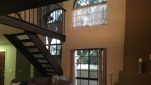 Un vaste espace de vie agrémenté d’un escalier menant à l’étage supérieur, d’une grande fenêtre avec des rideaux et d’une cheminée décorée de divers objets.
