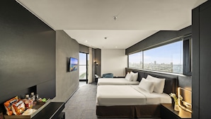Une chambre d’hôtel avec deux lits, une grande fenêtre donnant sur la ville, un téléviseur à écran plat et un minibar.