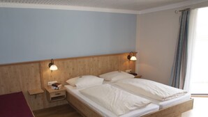 A double bed with wooden headboard and nightstands, a red blanket, and a window with curtains. - Vacation apartment Chiemsee, 65sqm, terrace, 1-5 persons (Übersee)