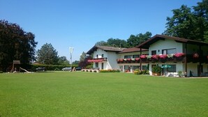 A large, well-maintained lawn in front of a two-story building with balconies adorned with flowers. - Vacation apartment Chiemsee, 65sqm, terrace, 1-5 persons (Übersee)