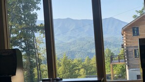 Una habitación con mesa de billar, ventanas amplias con vista a la montaña y una cabaña de madera al fondo.