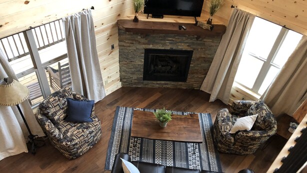 Una sala de estar acogedora con chimenea, dos sofás estampados, una mesa de centro y un televisor montado sobre la chimenea.