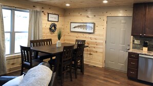Interior acogedor de una cabaña con comedor, paredes de madera, una puerta gris y una cocina con encimeras de granito.