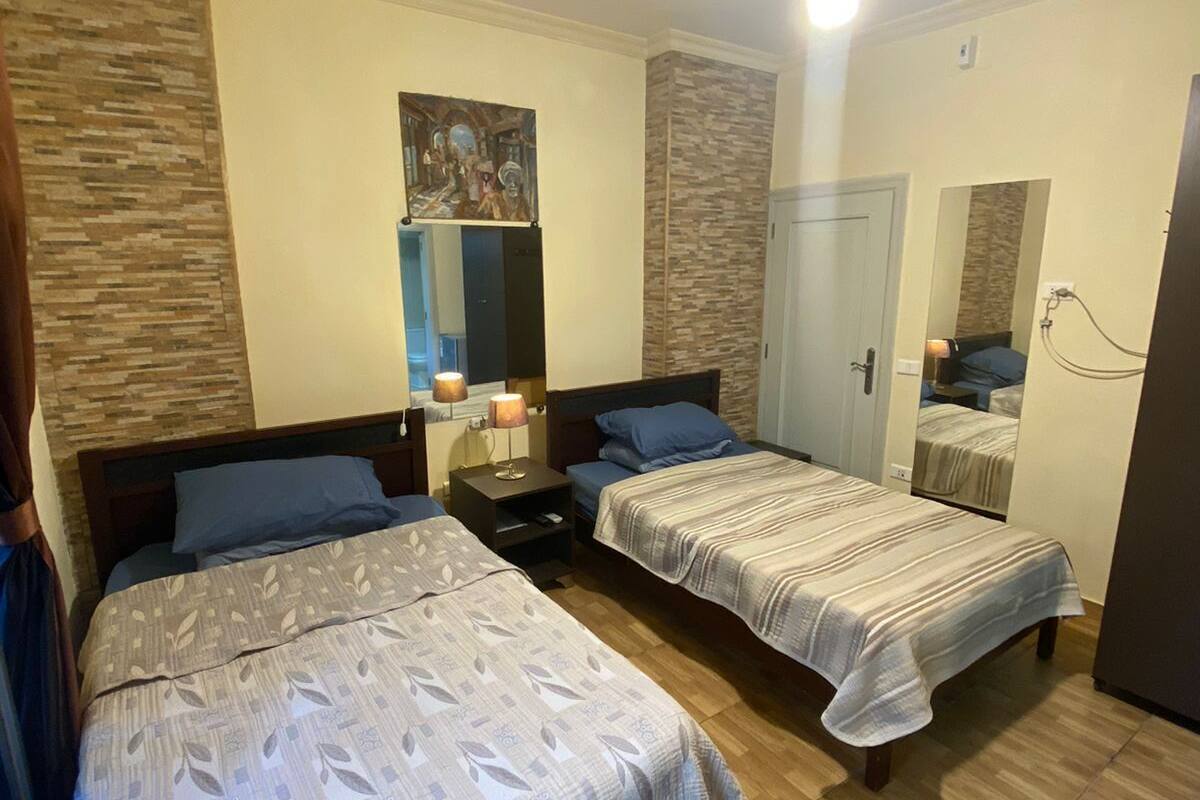 Habitación de hotel con dos camas, una mesita de noche, un espejo y un ventilador de techo.