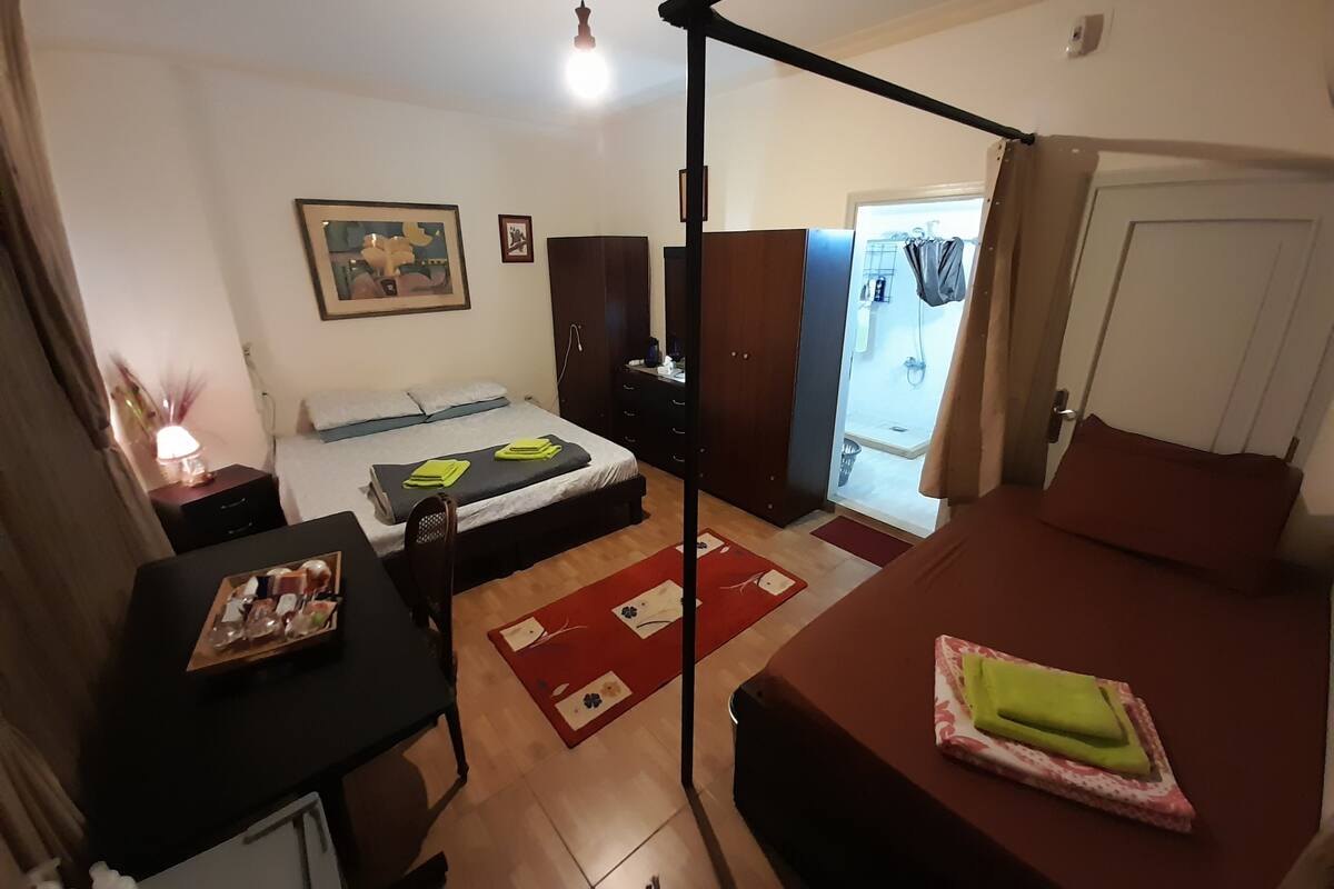 Un dormitorio pequeño con cama, mesita de noche y armario. También se observa un escritorio con silla y lámpara.