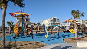 Ein Spielplatz mit bunten Spielgeräten und Palmen.