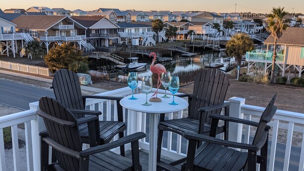 Eine Terrasse mit vier Adirondack-Stühlen und einem runden Tisch, mit Blick auf einen Yachthafen mit Booten und Häusern.