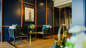 A modern interior with two black wicker sofas, a small table with a vase, and a framed picture of a famous landmark. - U Sabai Hotel (Bangkok)