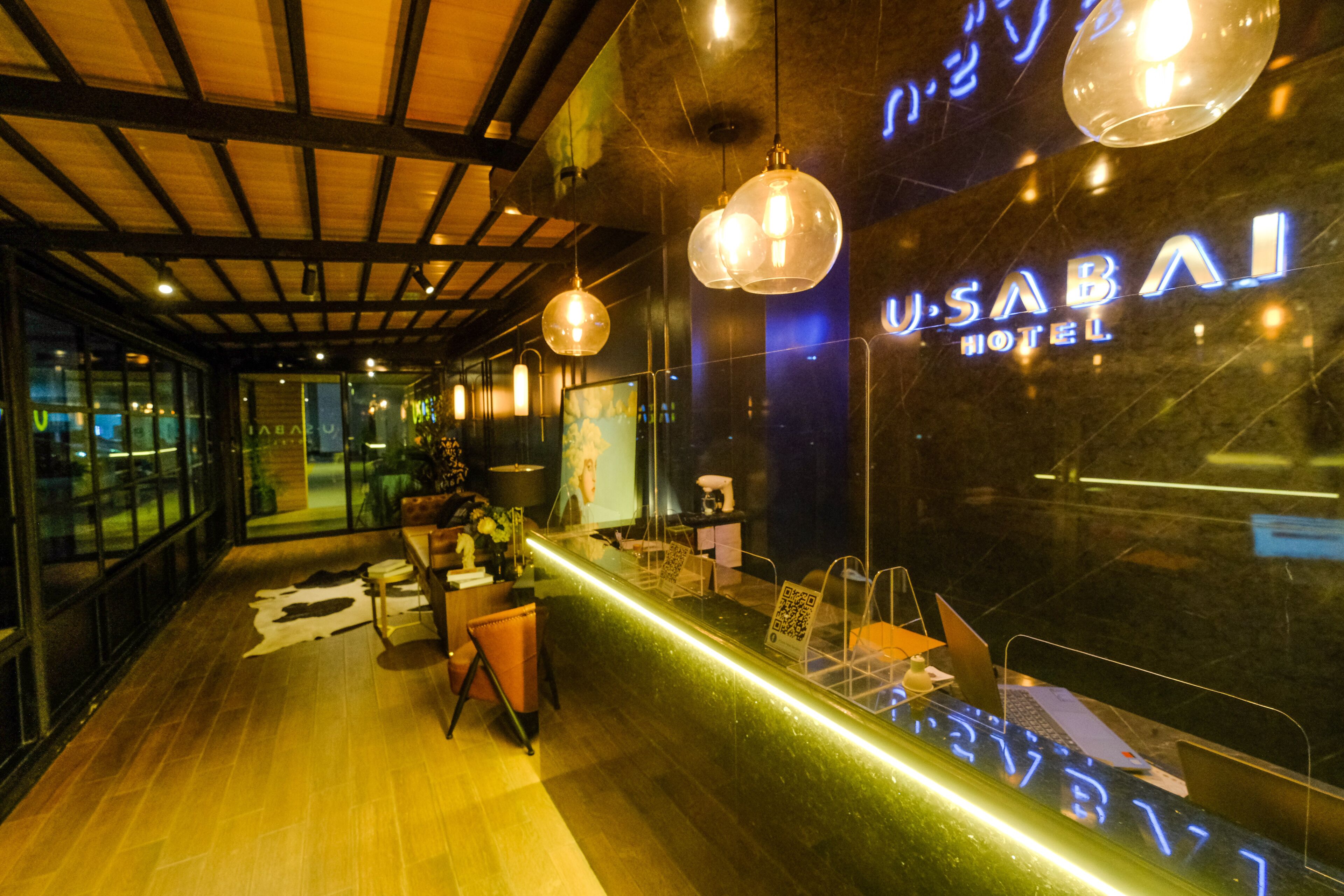 A reception area with a glass partition, a wooden floor, and a neon sign for the USABAI HOTEL.
