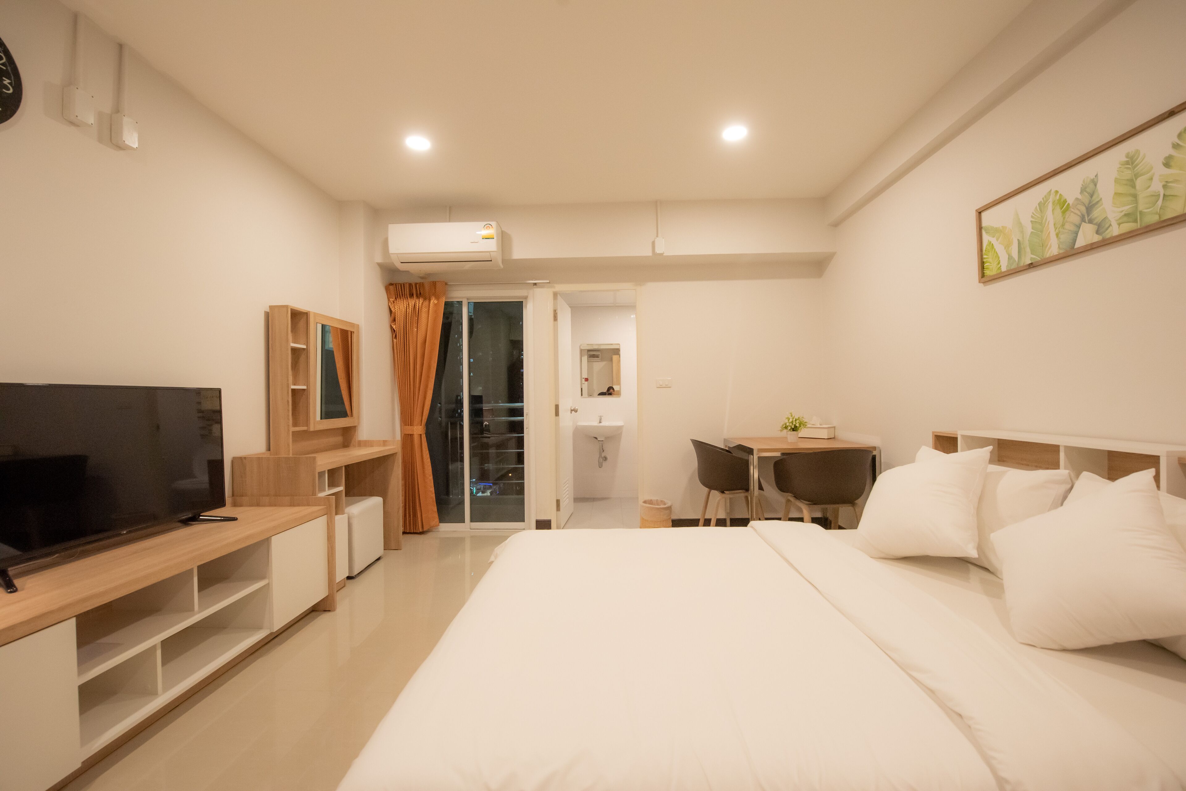 A modern hotel room with a large bed, a TV, a desk, and a bathroom visible through an open door.