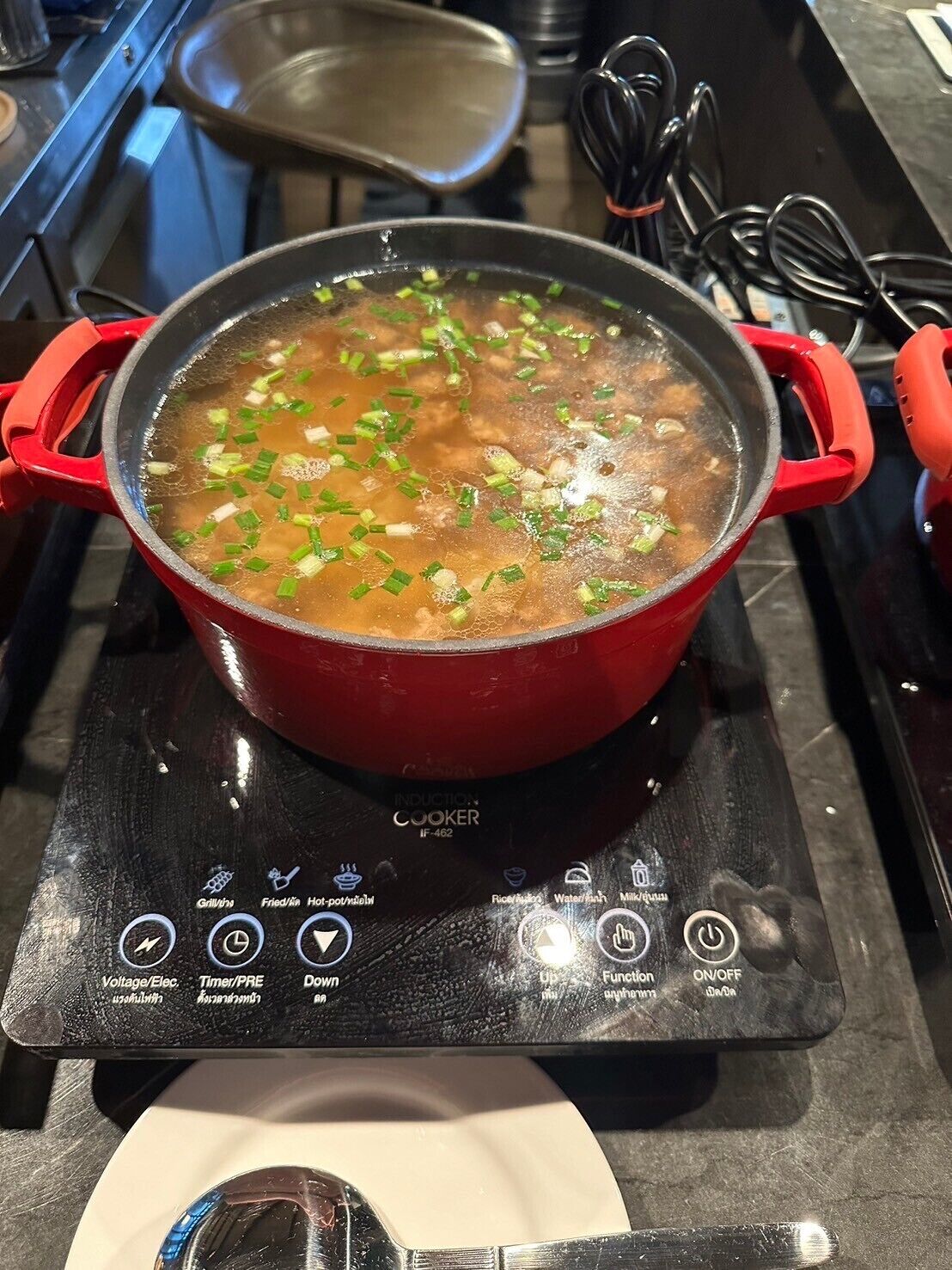 Una olla roja sobre una cocina de inducción con un panel de control digital que muestra diferentes opciones de cocción.
