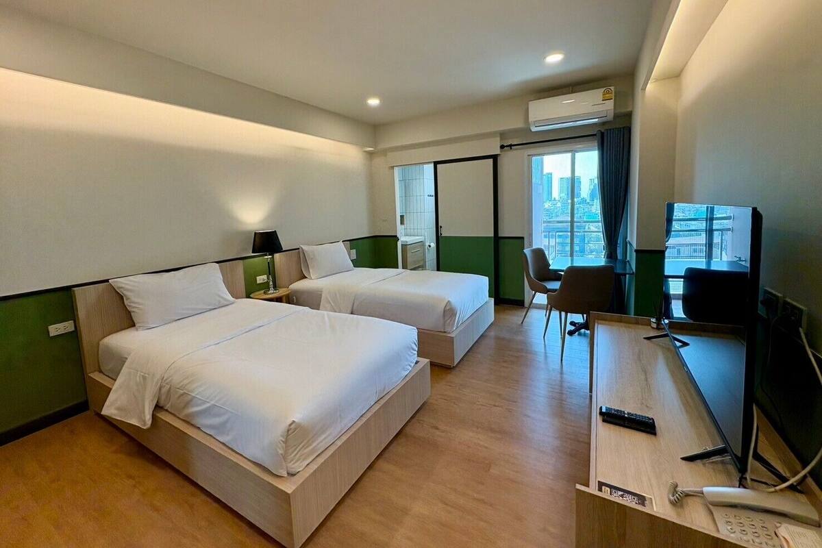 Quarto de hotel com duas camas, uma mesa com computador, uma cadeira e vista para a cidade.