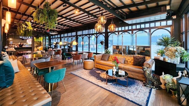 A spacious lounge area with a high ceiling, wooden beams, and large windows offering a view of the outside. - U Sabai Hotel (Bangkok)