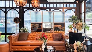 A cozy living room with a leather sofa, a coffee table, and a large window with a view of the city. - U Sabai Hotel (Bangkok)