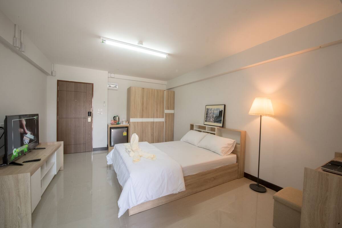 Quarto de hotel moderno com cama, mesa de cabeceira, televisão e luminária.
