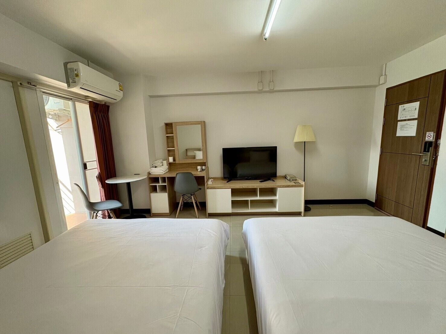 A hotel room with two beds, a desk with a TV, a chair, a lamp, and a wardrobe.