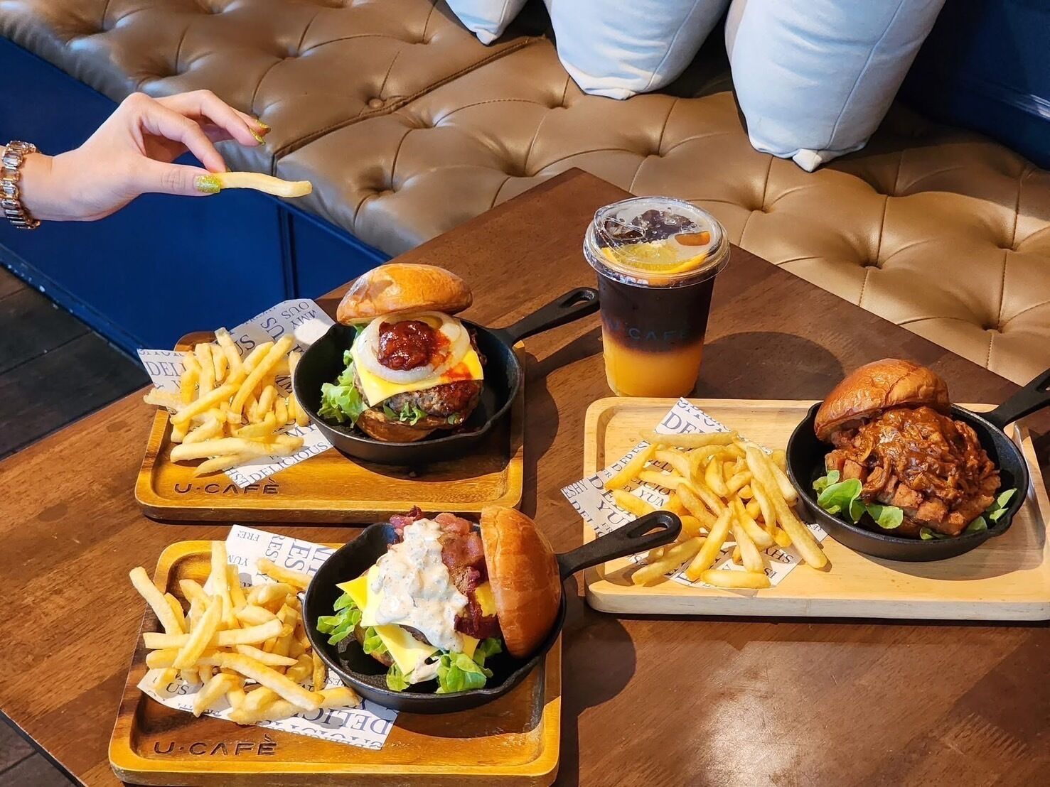 A dining table with three meals: burgers, fries, and a drink.