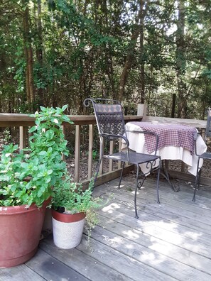 A wooden deck with a table and chairs, surrounded by lush greenery. -  2-Story Farm Cabin - Sleeps 5 - 50 Acres (Flint)