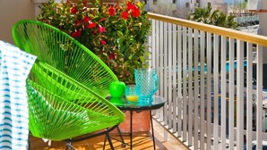 A balcony with a green chair, a small table with a glass vase, and a view of the sea and buildings. - A. Corales del Mar in Alcudia Beach (Port d´Alcudia)