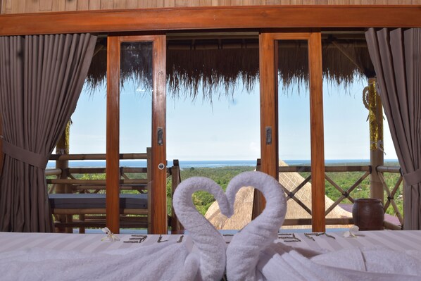Una habitación con una cama, una puerta de madera y vista al océano.