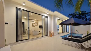 A modern house with a swimming pool, large sliding glass doors, and a lounge area with a sun umbrella. - The Grand Daha Luxury Villas (Seminyak)