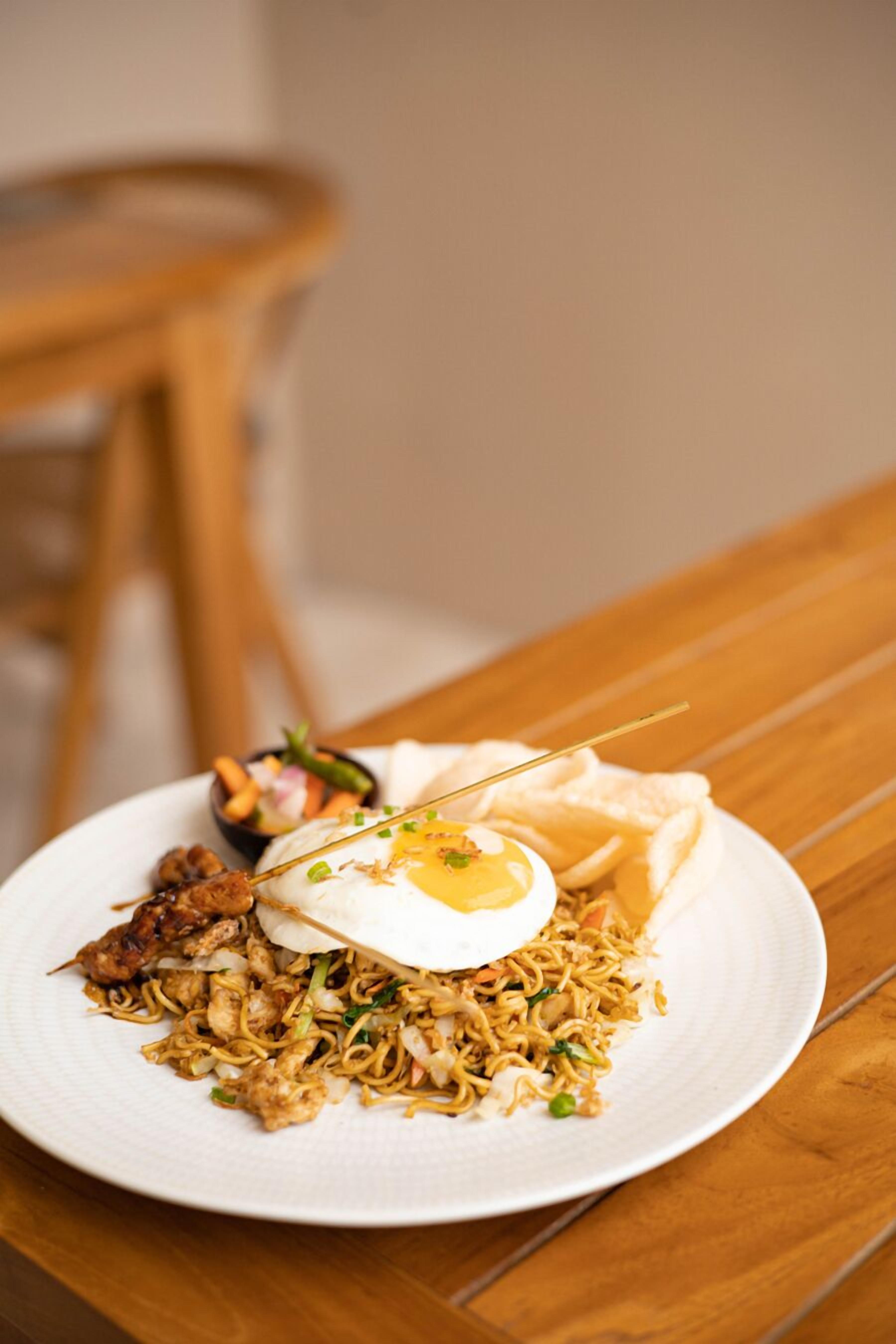 A plate of stir-fried noodles with vegetables and a boiled egg on a white plate.