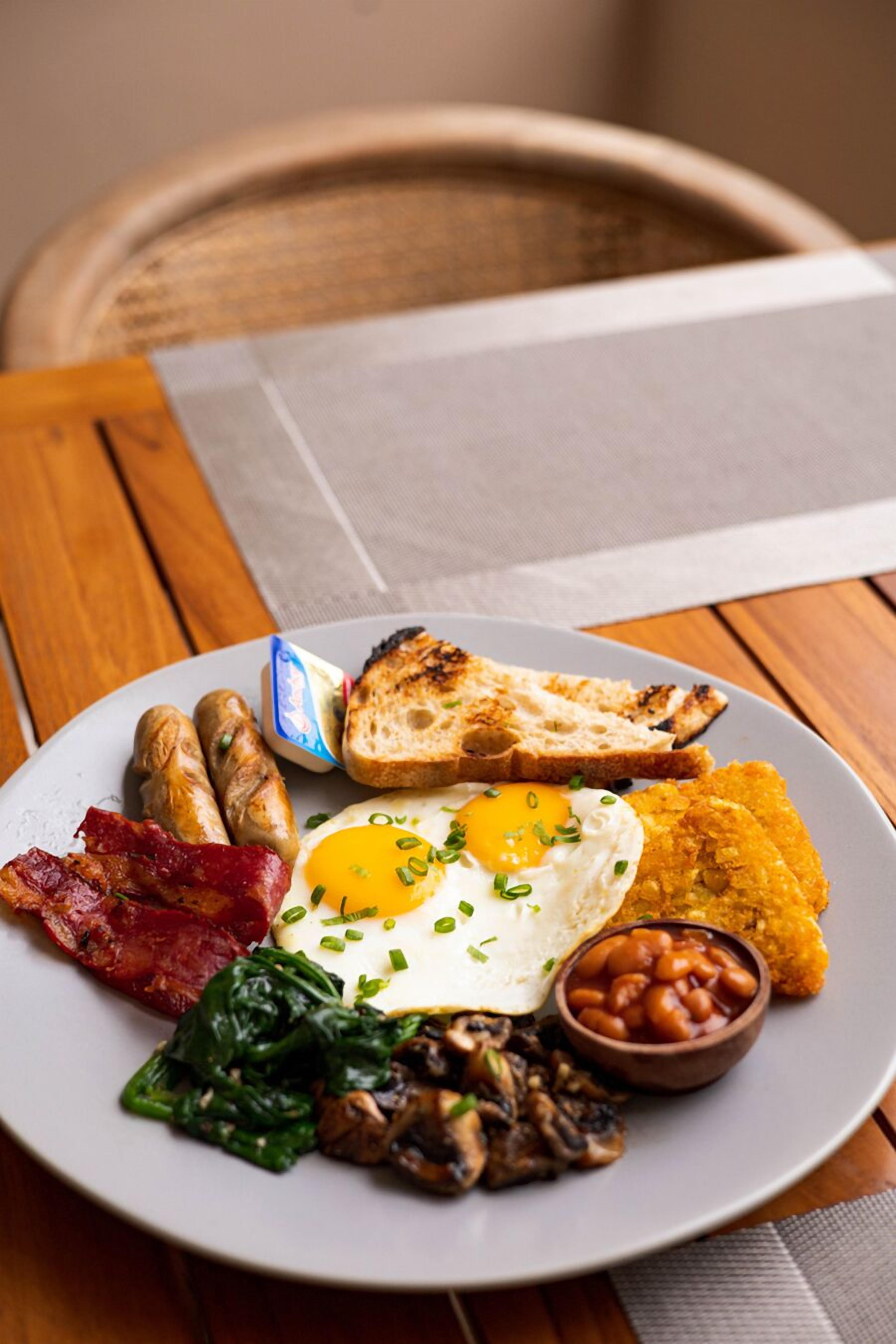 A plate of breakfast food including eggs, sausages, toast, beans, and greens.