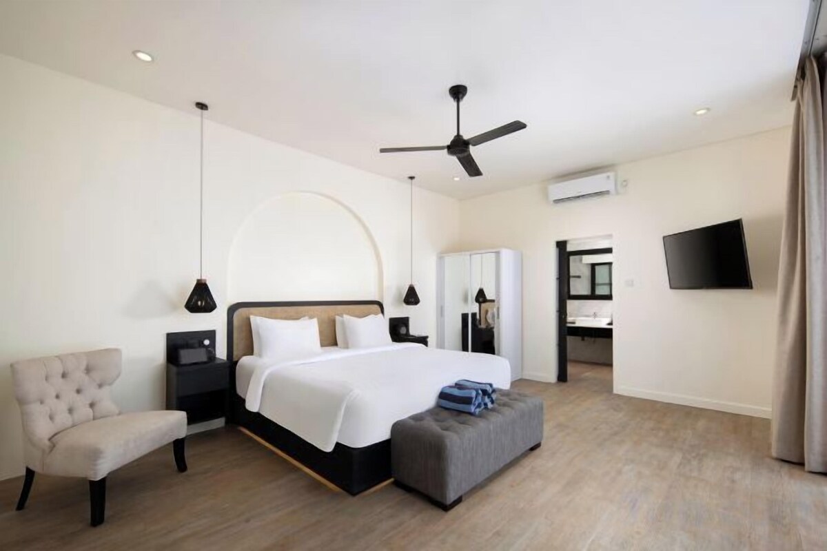 A modern hotel room with a bed, bedside table, chair, and a flat-screen TV.