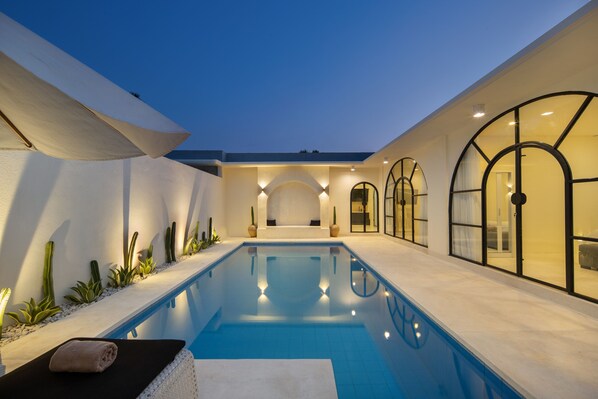 Un área de piscina interior moderna con una piscina cristalina, sillas de descanso y un espacio para sentarse.