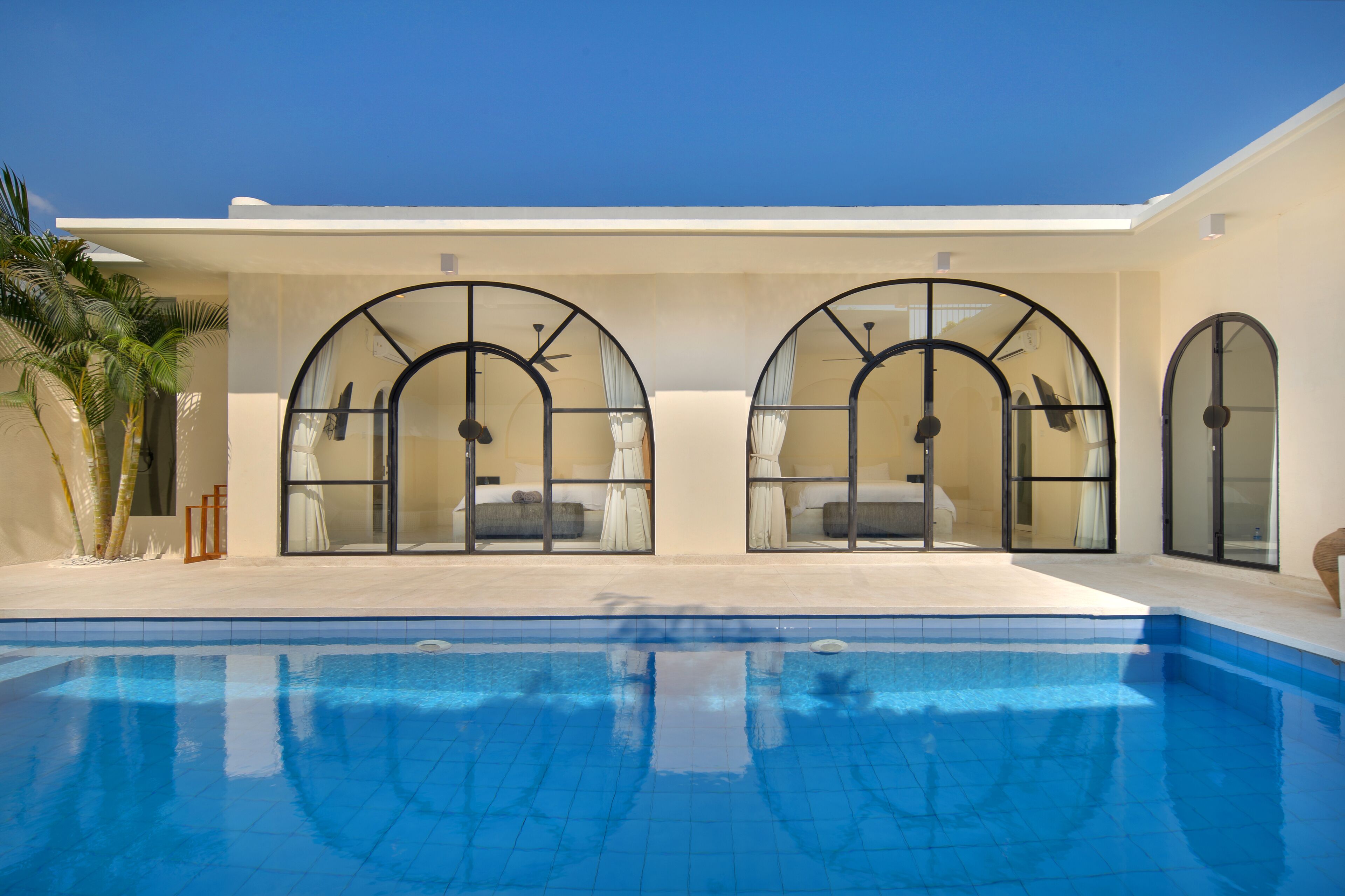 A modern hotel with a pool, large arched windows, and a minimalist design.