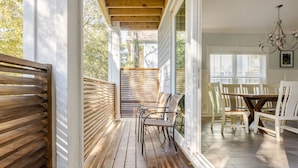 Un área de estar al aire libre techada, con bancos de madera y una mesa, rodeada por puertas y ventanas de vidrio.