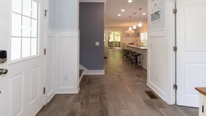 Un pasillo con suelo de madera, puertas blancas y una zona de cocina con taburetes de bar.