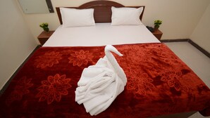 A neatly made bed with a red floral bedspread, white pillows, and a white towel folded on the bed. - Hotel Kashi Khand (Varanasi)