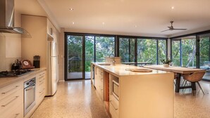A modern kitchen with a large island, stainless steel appliances, and large windows offering a view of the outdoors. - Carpe Vino - Peaceful Bushland Luxury Between Coast and Town (Margaret River)