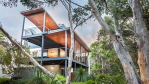 A modern, multi-level house with a glass facade, surrounded by lush greenery and trees. - Carpe Vino - Peaceful Bushland Luxury Between Coast and Town (Margaret River)
