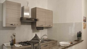 Eine moderne Küche mit hellen Holzschränken, einer Edelstahl-Dunstabzugshaube, einer Granit-Arbeitsplatte und einer kleinen Kochinsel mit Spüle.