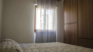 Ein Schlafzimmer mit Bett, Kleiderschrank und einem Fenster mit Vorhängen.