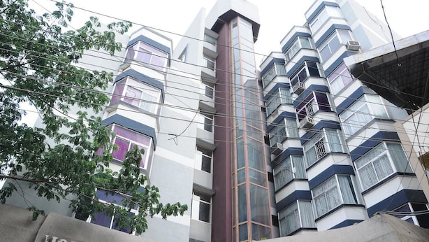 A modern hotel building with multiple floors, large windows, and a prominent central tower. - Hotel Raamus (Coimbatore)