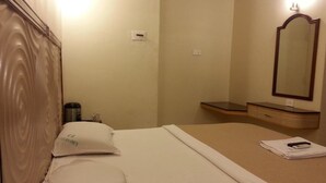 A hotel room with a bed, a bedside table, a mirror, and a small cabinet. - Hotel Raamus (Coimbatore)