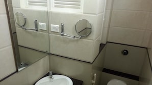 A compact bathroom with a white sink, a mirror, a toilet, and a window with blinds. - Hotel Raamus (Coimbatore)