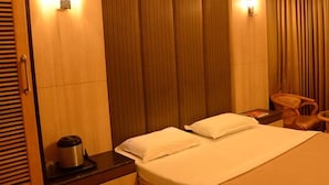 A hotel room with a bed, a nightstand, a chair, a small table, and a curtain. - Hotel Raamus (Coimbatore)