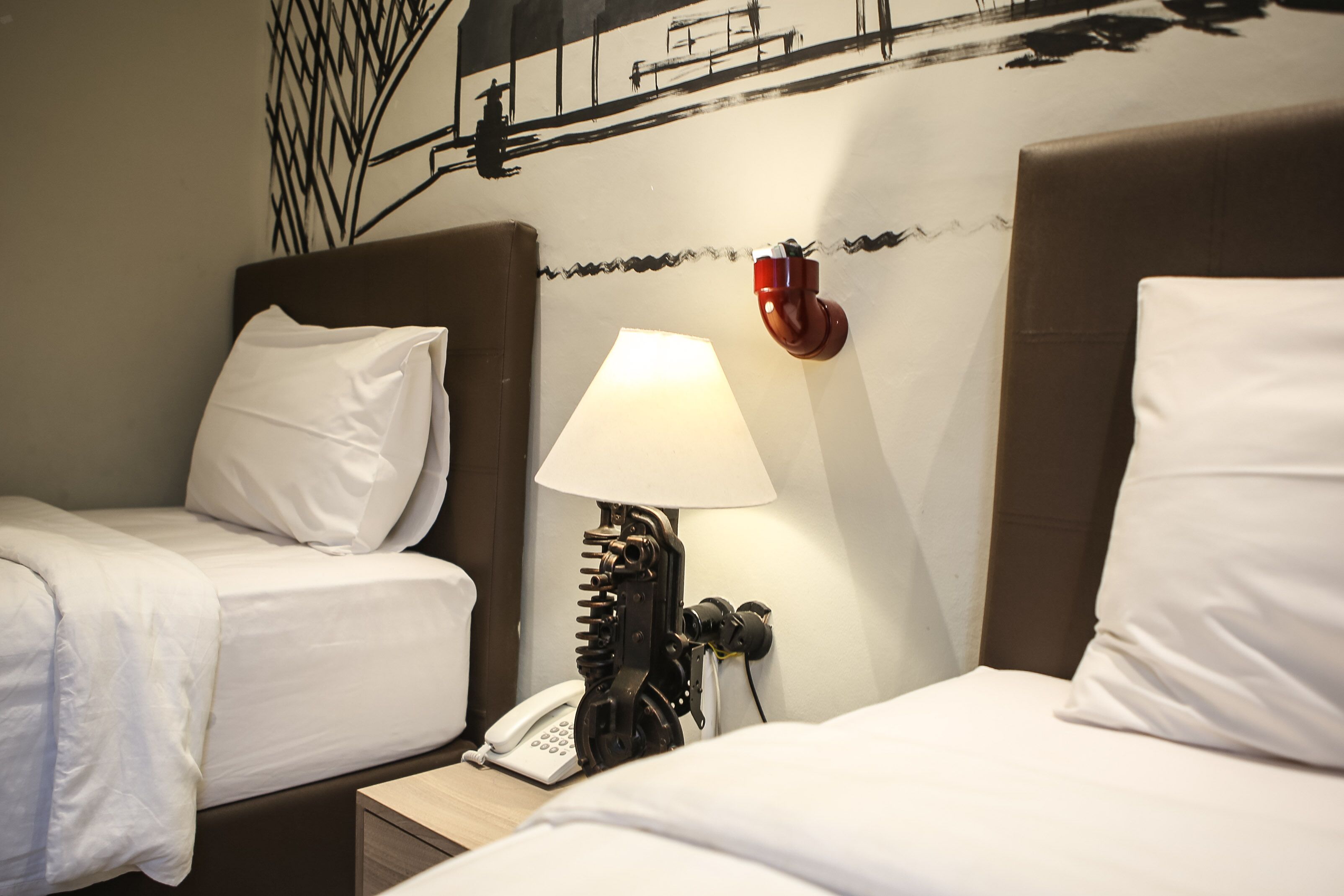 A hotel room with two beds, a wall-mounted telephone, and a unique wall-mounted lamp.