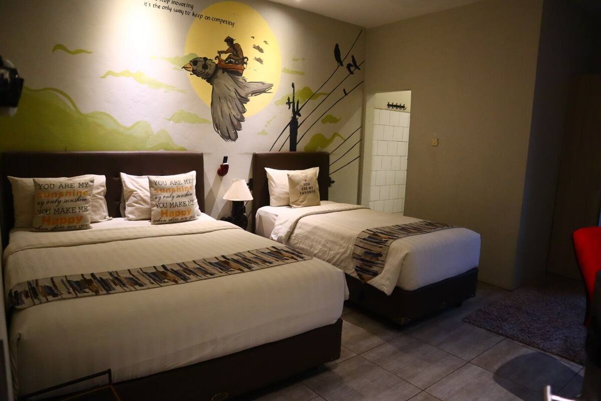 A hotel room with two beds, a mural on the wall, and a red chair.