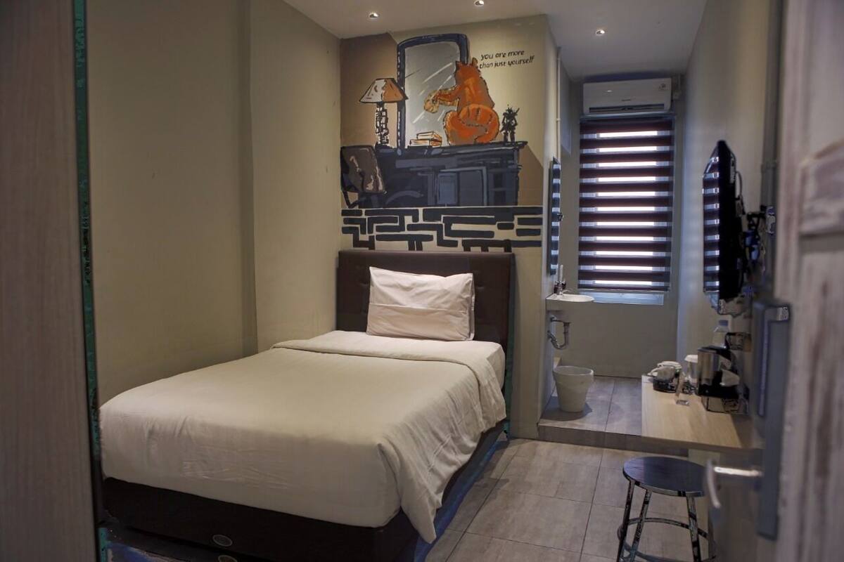 A bedroom with a bed, a desk, a chair, a mirror, and a window with blinds.
