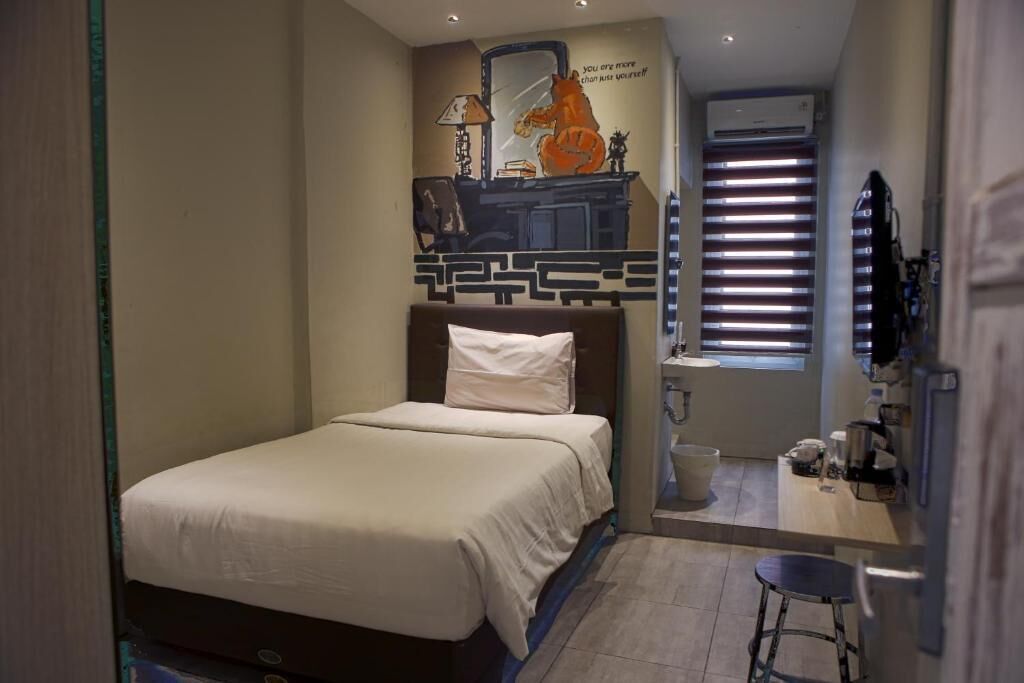 Une chambre à coucher avec un lit, un bureau avec une chaise, un miroir et une fenêtre avec des stores.