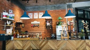 Interior de una cafetería con mostrador de madera en diseño espiga, luces colgantes azules y una pared de ladrillo.