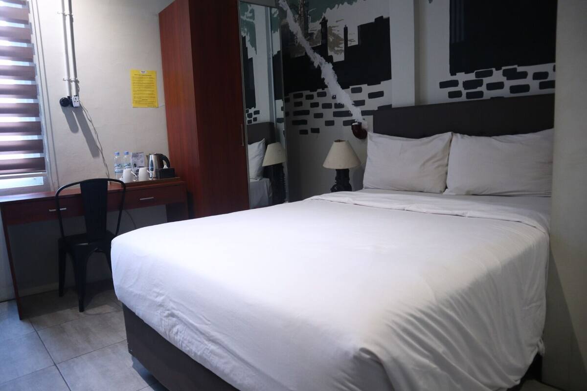 A hotel room with a bed, desk, chair, and a cityscape mural on the wall.