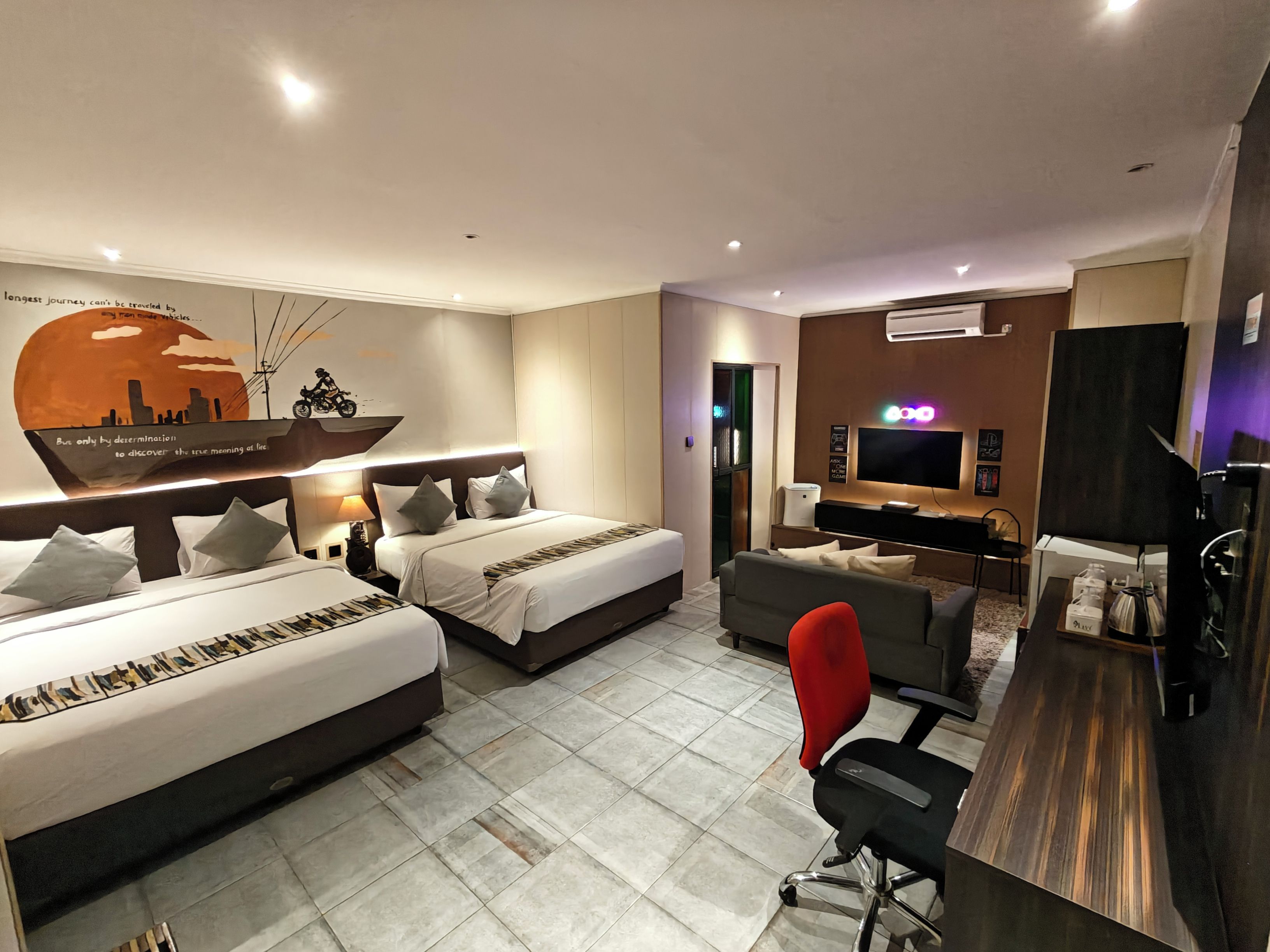 A hotel room with two beds, a desk, a TV, and a wall with a cityscape mural.